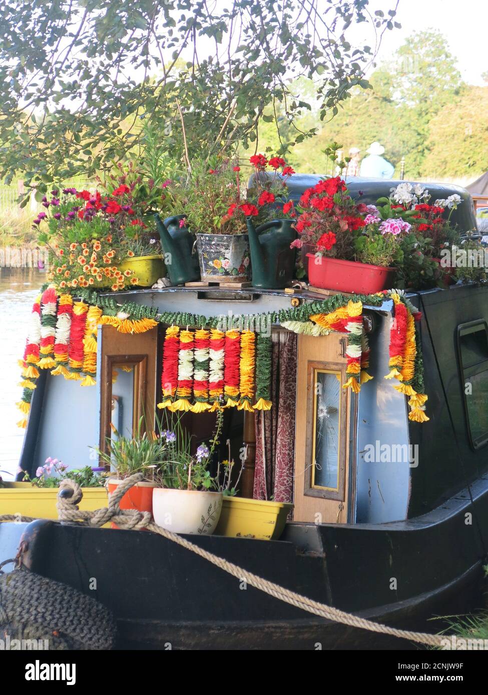 The colourful stern of an English narrowboat on the Grand Union Canal, decorated with pots of red geraniums and garlands of bright paper flowers. Stock Photo