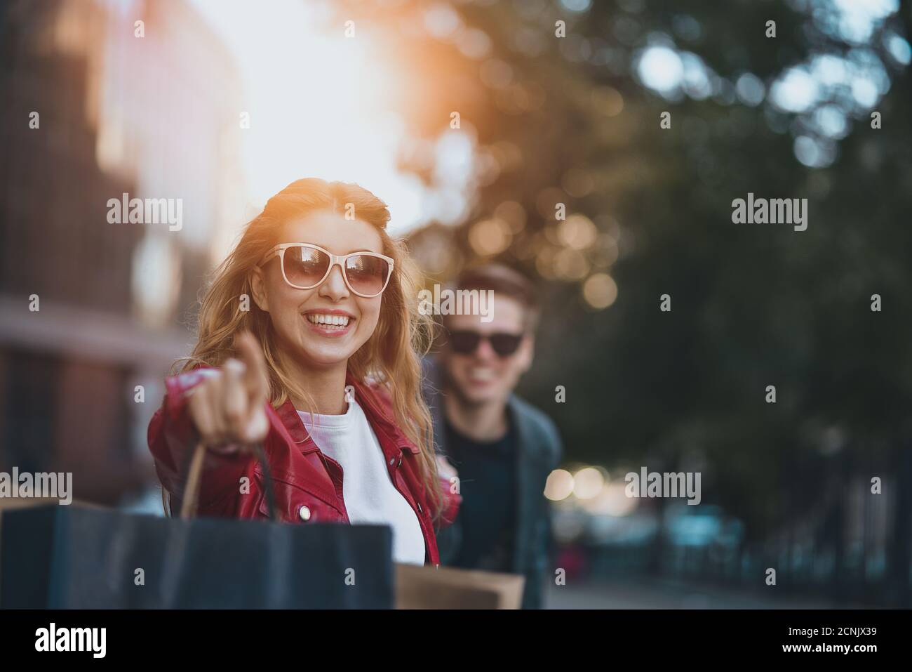 Front view of a casual couple of shoppers running in the street towards camera holding colorful shopping bags. Stock Photo