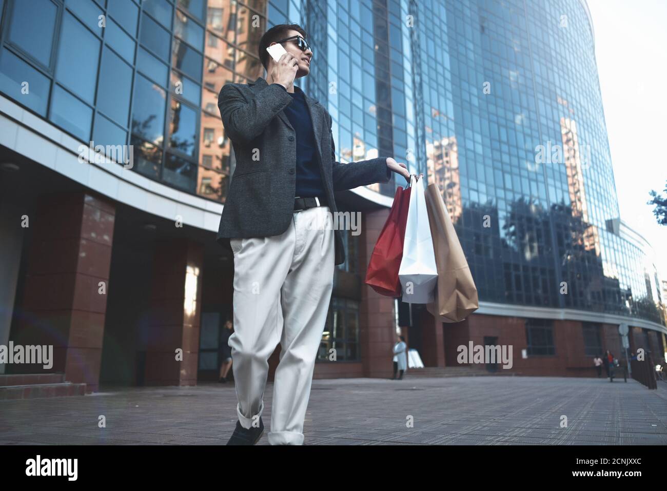 Happy stylish young man with phone walking in urban street and enjoying Black Friday shopping in trendy stores in city. Stock Photo