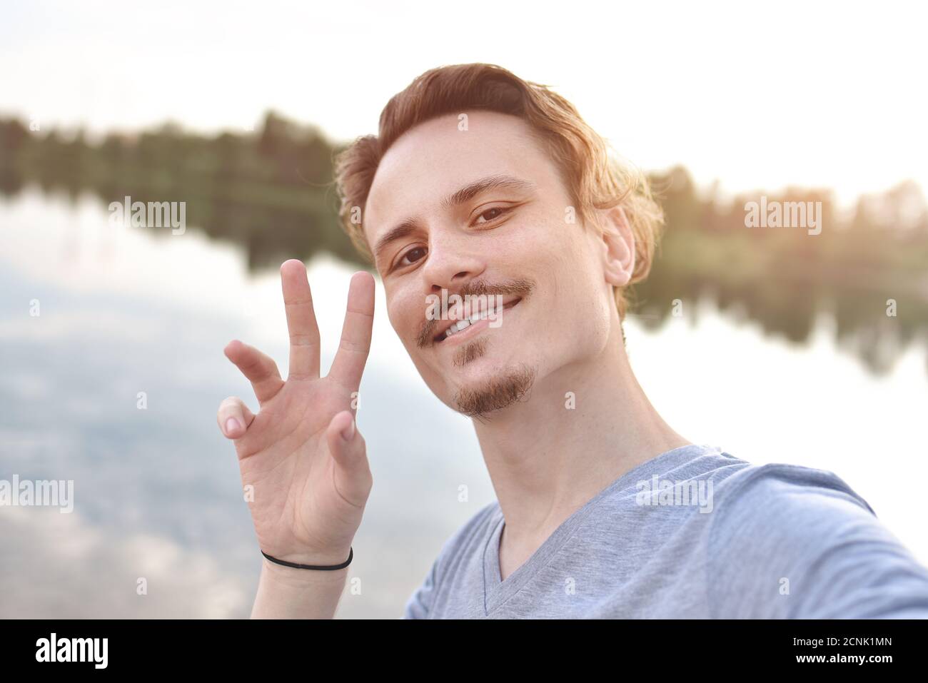 portrait of Young handsome stylish smiling guy makes selfie against the lake. peace sign Stock Photo