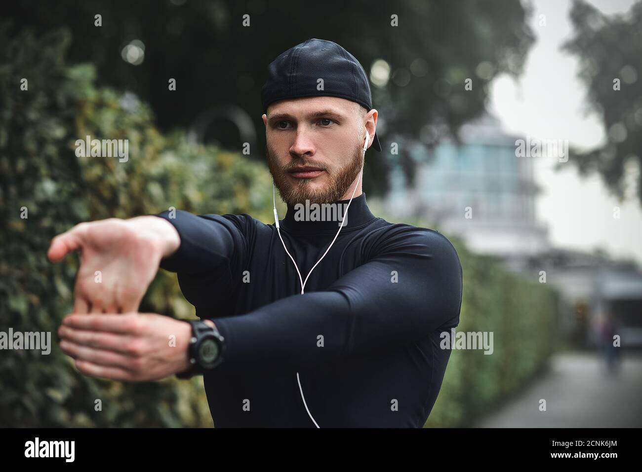 Muscular sportsman stretching out before a sports training at the street in city park Stock Photo