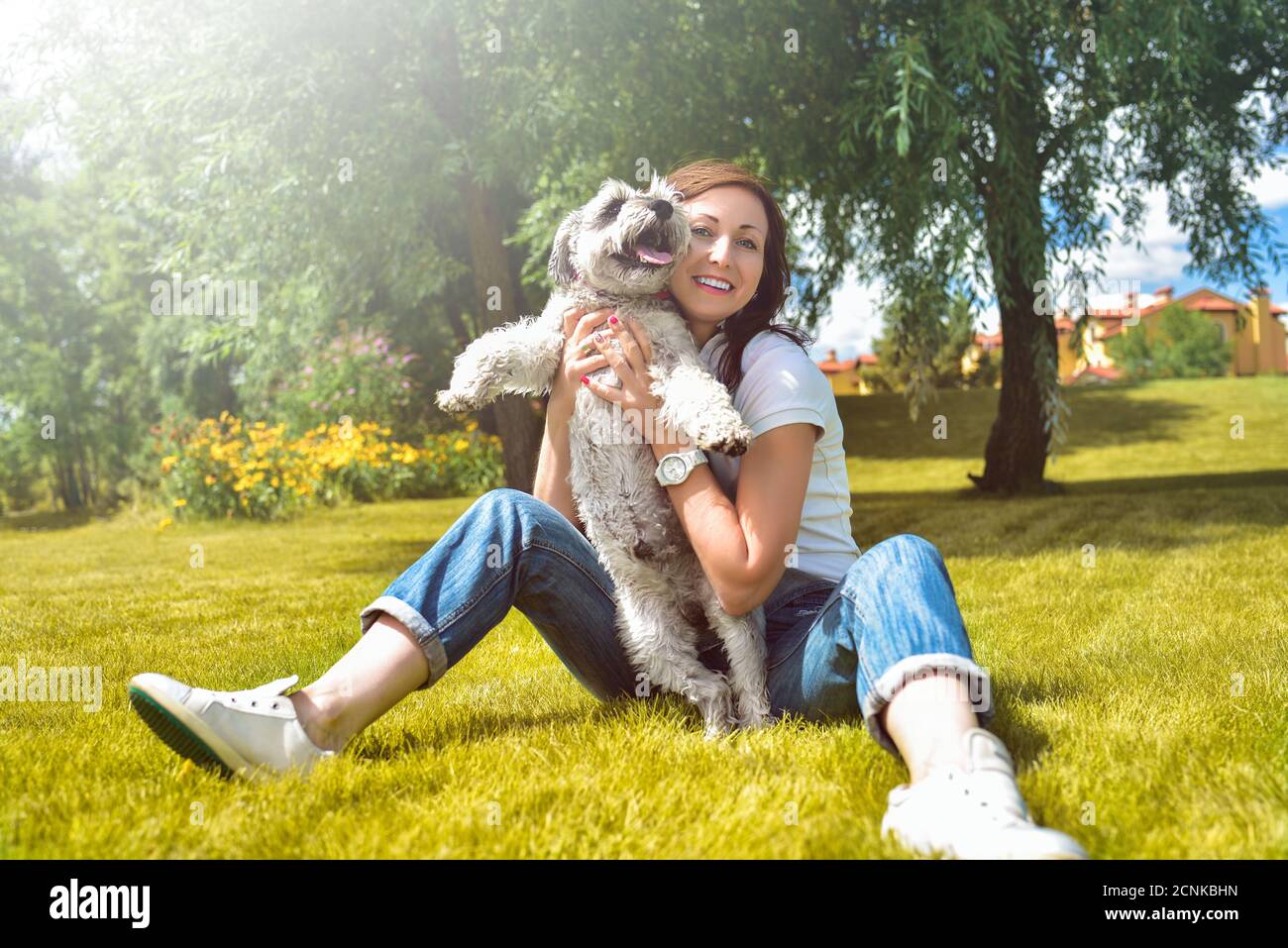 Pretty adult caucasian happy woman resting in the park on a sunny day with her beloved dog. Female lies on the grass, smiling an Stock Photo