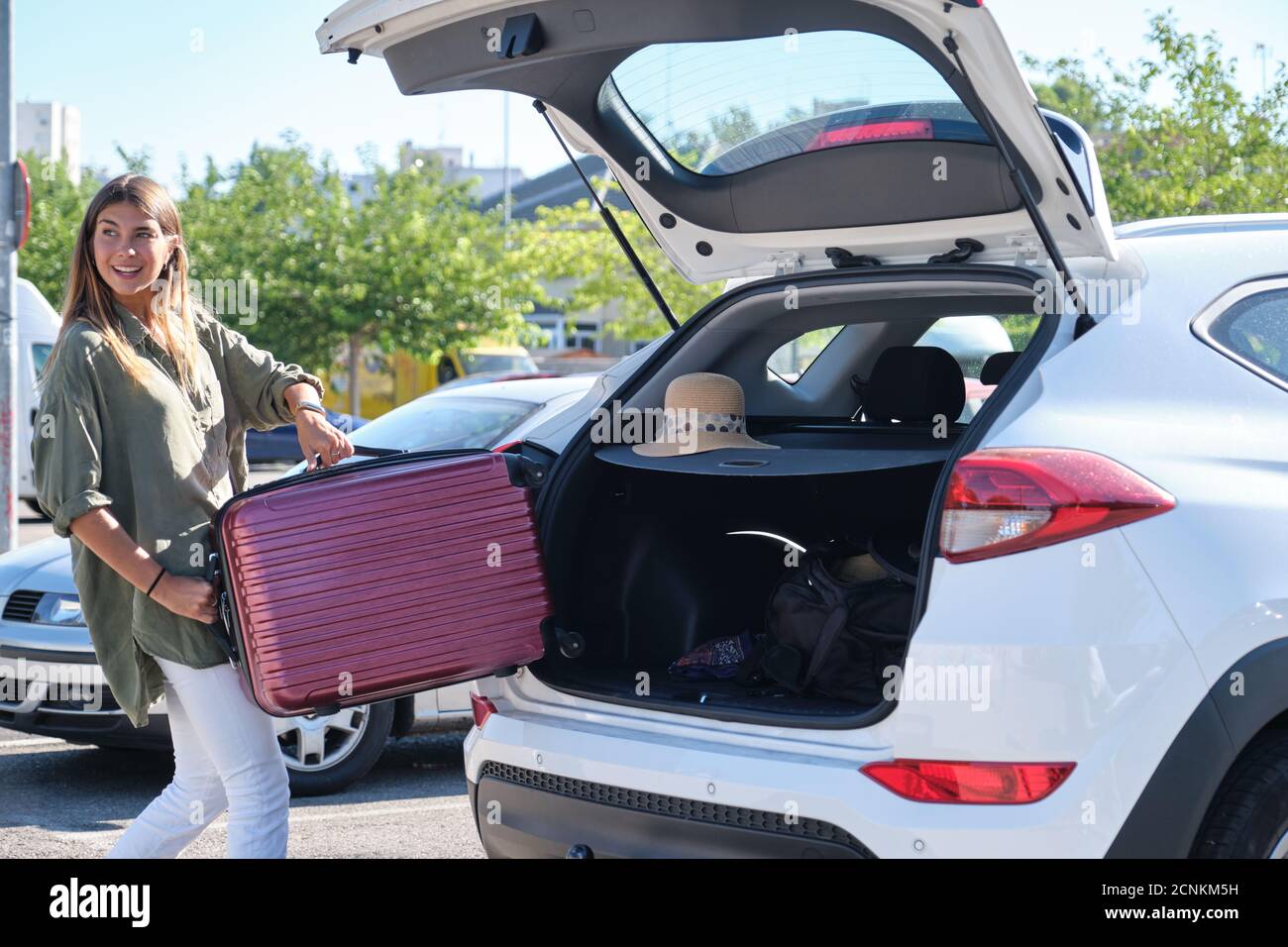 Young happy woman packing her suitcase into luggage boot of the car ...