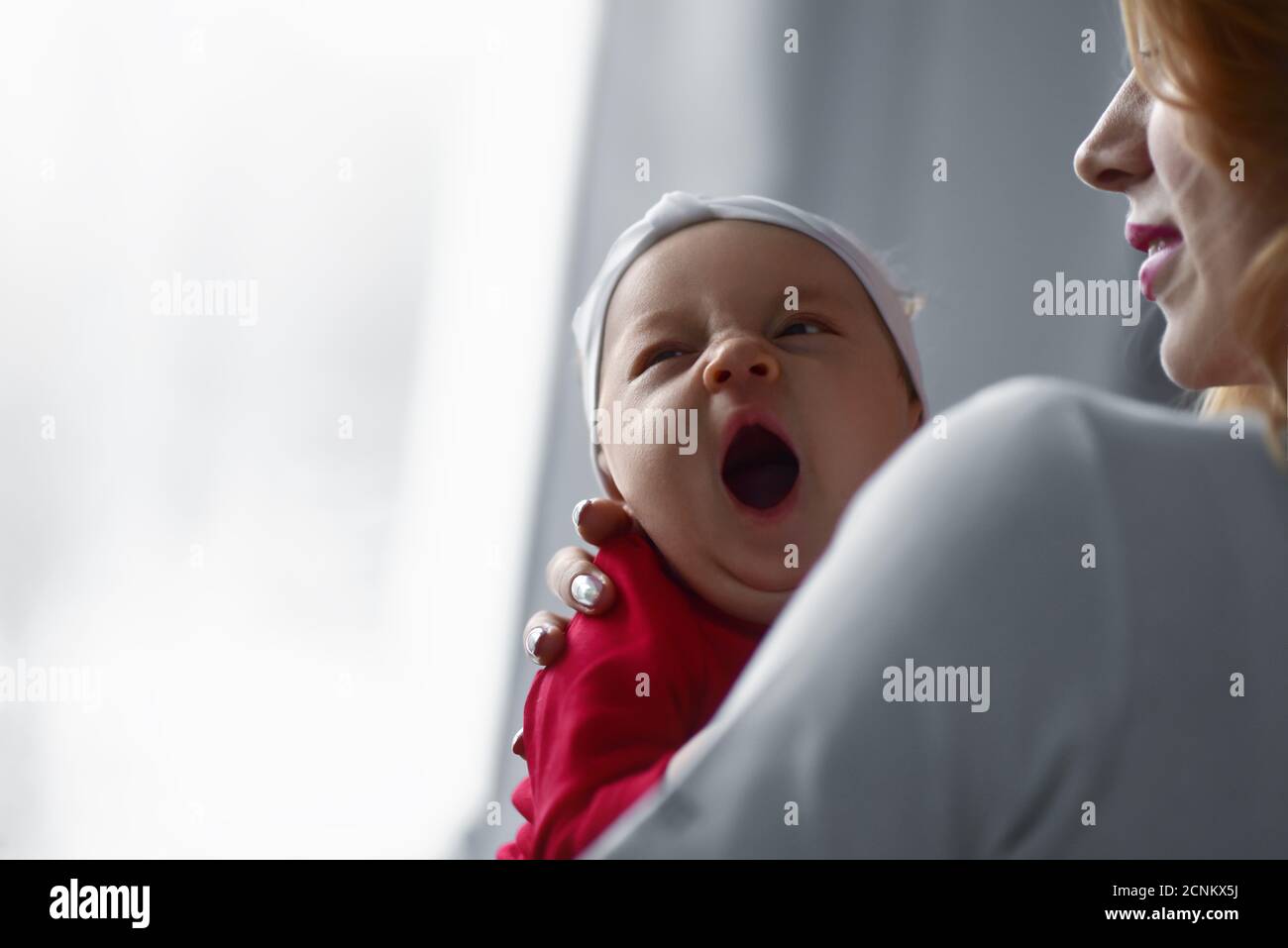 Mother holding cute newborn baby girl in her arms. Sleepy baby yawning. Stock Photo