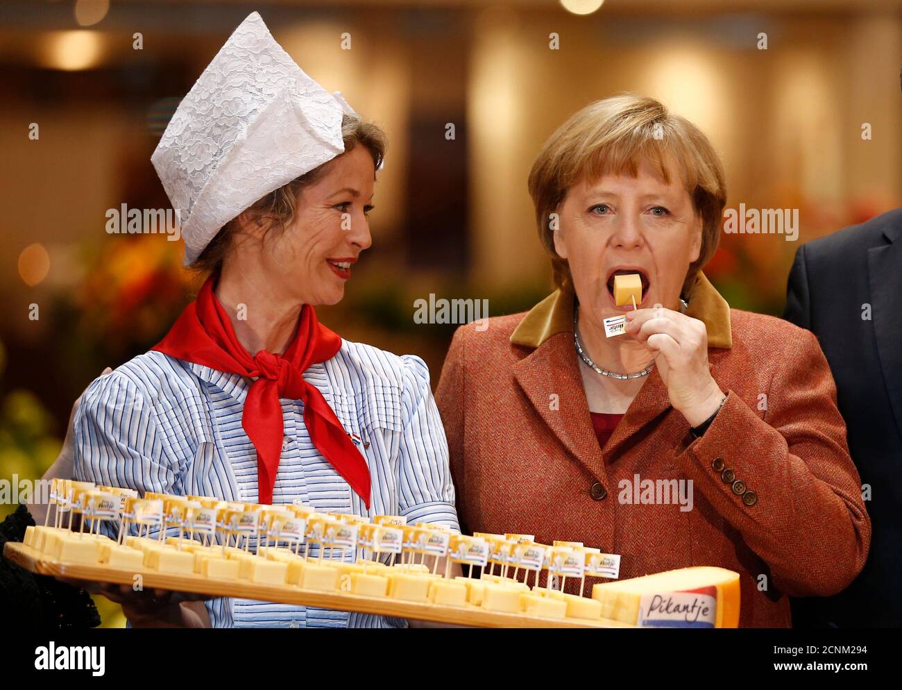 German Chancellor Angela Merkel (R) samples cheese at the pavilion of the Netherlands at the Green Week agricultural fair in Berlin, January 18, 2013. The Netherlands are the partner nation of the Green Week this year.  REUTERS/Thomas Peter  (GERMANY  - Tags: POLITICS AGRICULTURE) Stock Photo