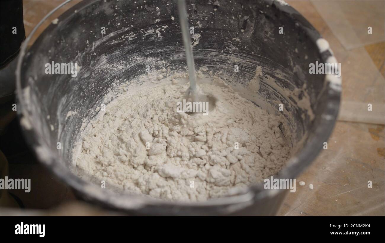 Builder mixing plaster in a bucket using an electric mixer. Builder