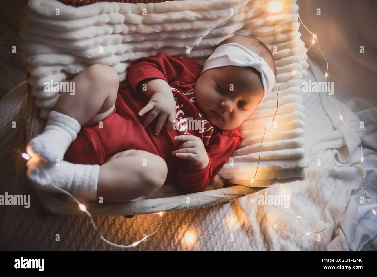 Little slipping baby boy with christmas clothes in basket christmas decoration and flash lights around her. Stock Photo