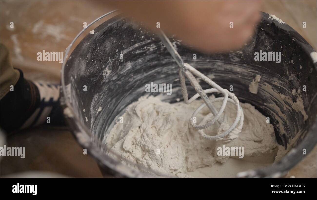 Builder mixing plaster in a bucket using an electric mixer. Builder