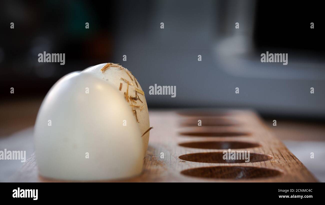 Straw covered fresh hens egg hiding behind another in wooden holder in