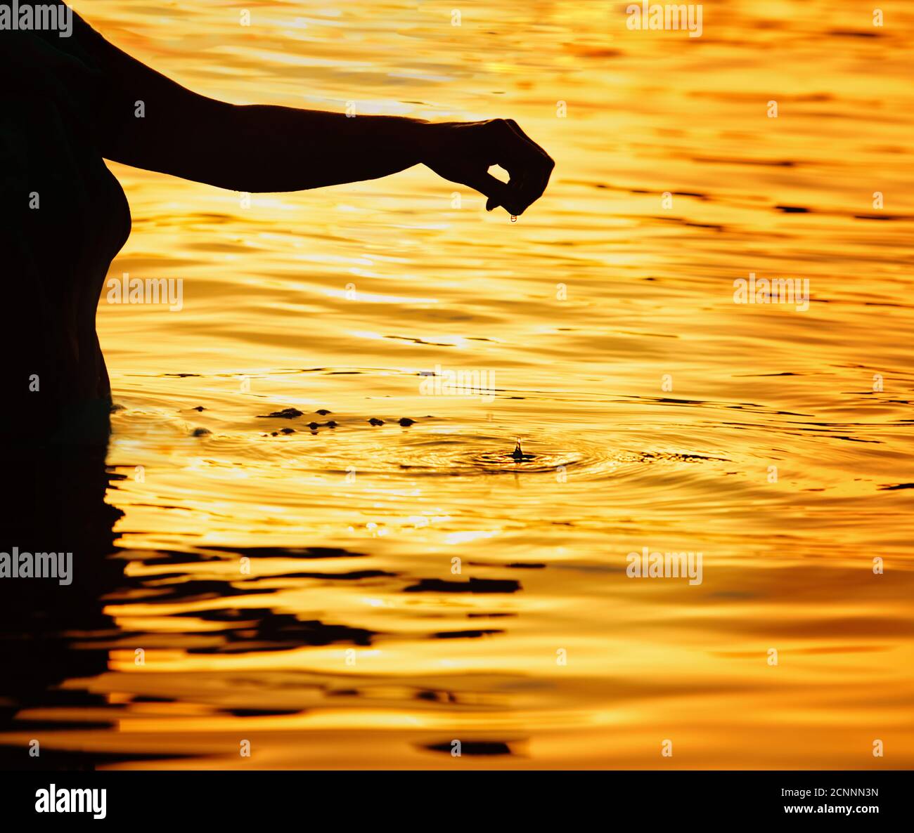 Silhouette of a woman standing in sea at sunset with her arm ...