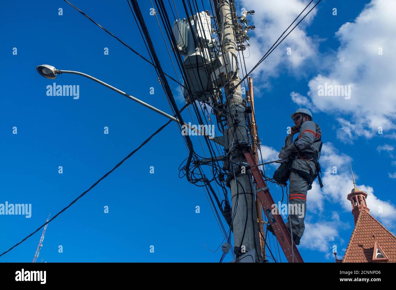 Worker of the electricity distribution company on top of utility pole. Stock Photo