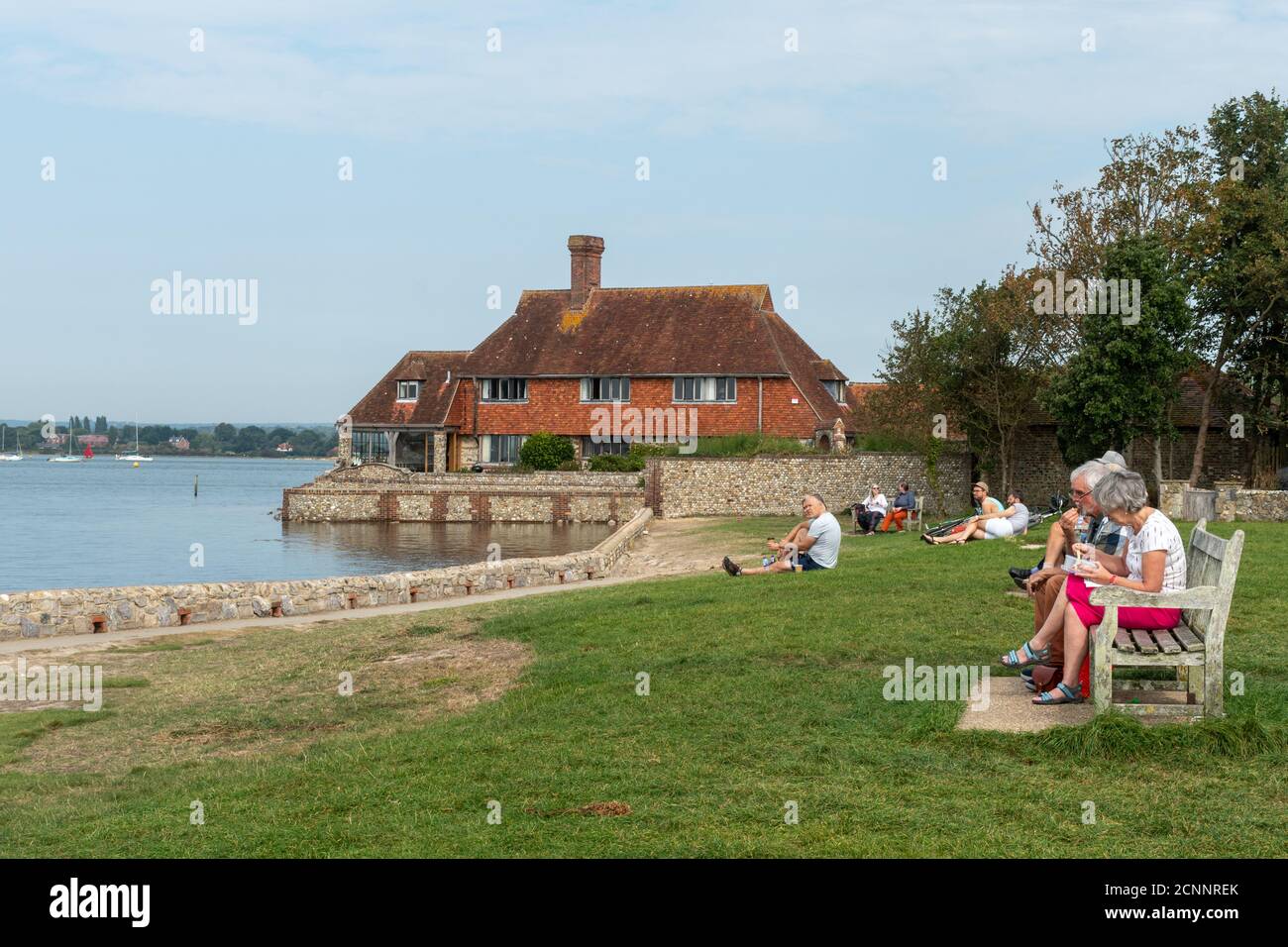 Visitors sitting and having picnics on the lawn overlooking Bosham Quay, a picturesque seaside village in West Sussex, UK Stock Photo