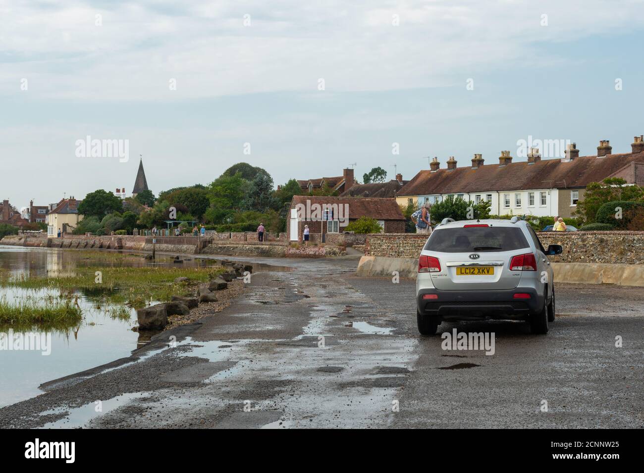 Car driving along the tidal shore road just after the tide has gone out, Bosham village, West Sussex, UK Stock Photo