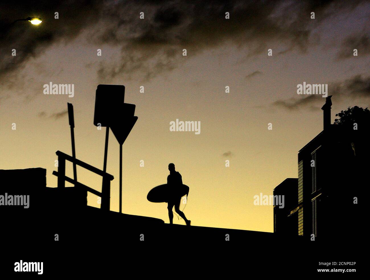 A surfer crosses the road with his board at sunset above Sydney's Bondi Beach June 16, 2005. Many local surfers continue to catch waves at the world-famous beach until well after sunset, and then walk back to their homes in their wetsuits to keep them warm in the winter months. REUTERS/David Gray  DG/TC Stock Photo