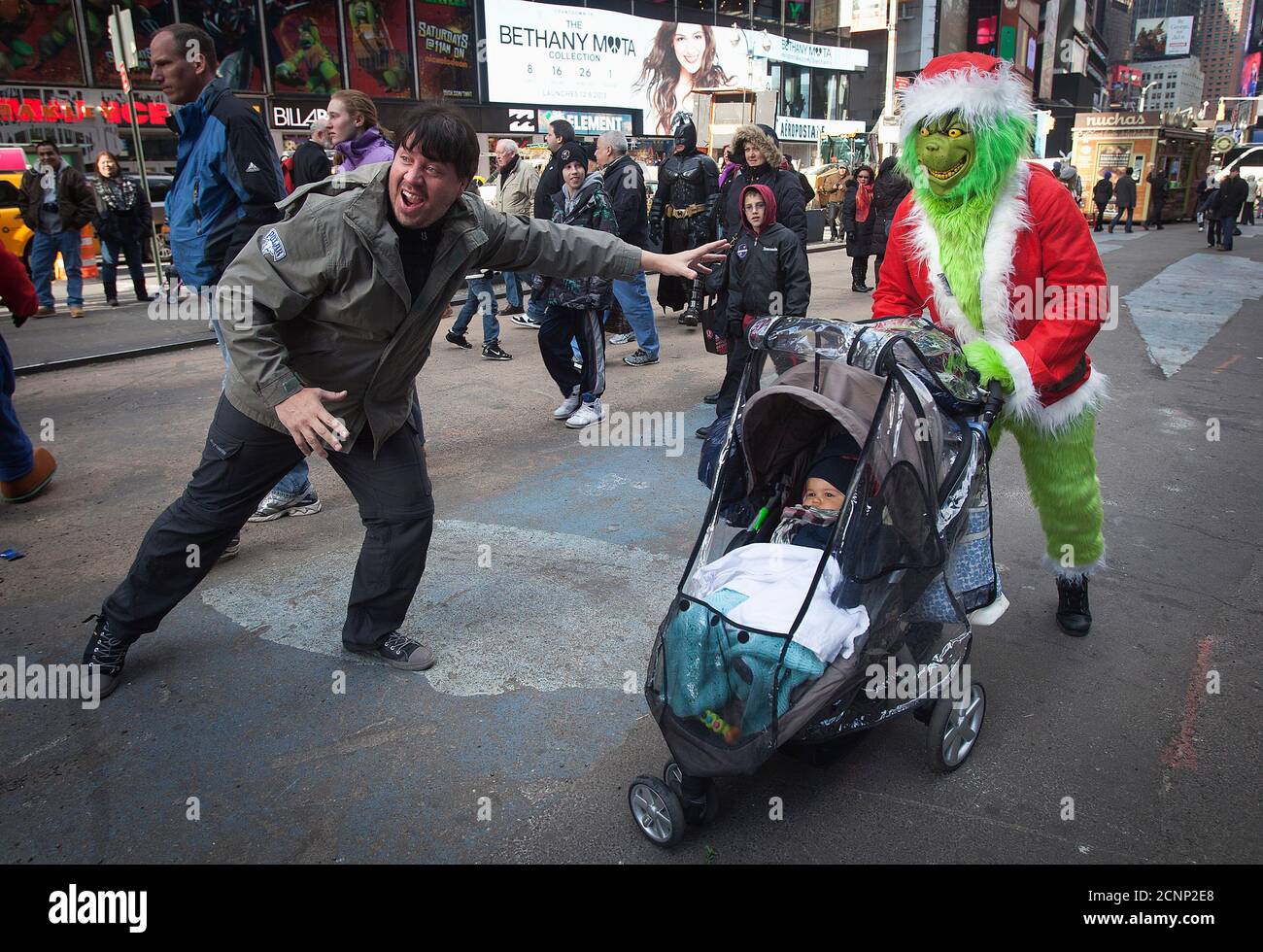 A man (R) dressed up as 'the Grinch', a fictional character by author Dr. Seuss, who poses for photos with people for money, poses for a picture with a baby in a stroller and his father in Times Square, during Black Friday sales in New York November 29, 2013. Black Friday, the day following Thanksgiving Day holiday, has traditionally been the busiest shopping day in the United States. REUTERS/Carlo Allegri (UNITED STATES - Tags: BUSINESS SOCIETY TPX IMAGES OF THE DAY) Stock Photo