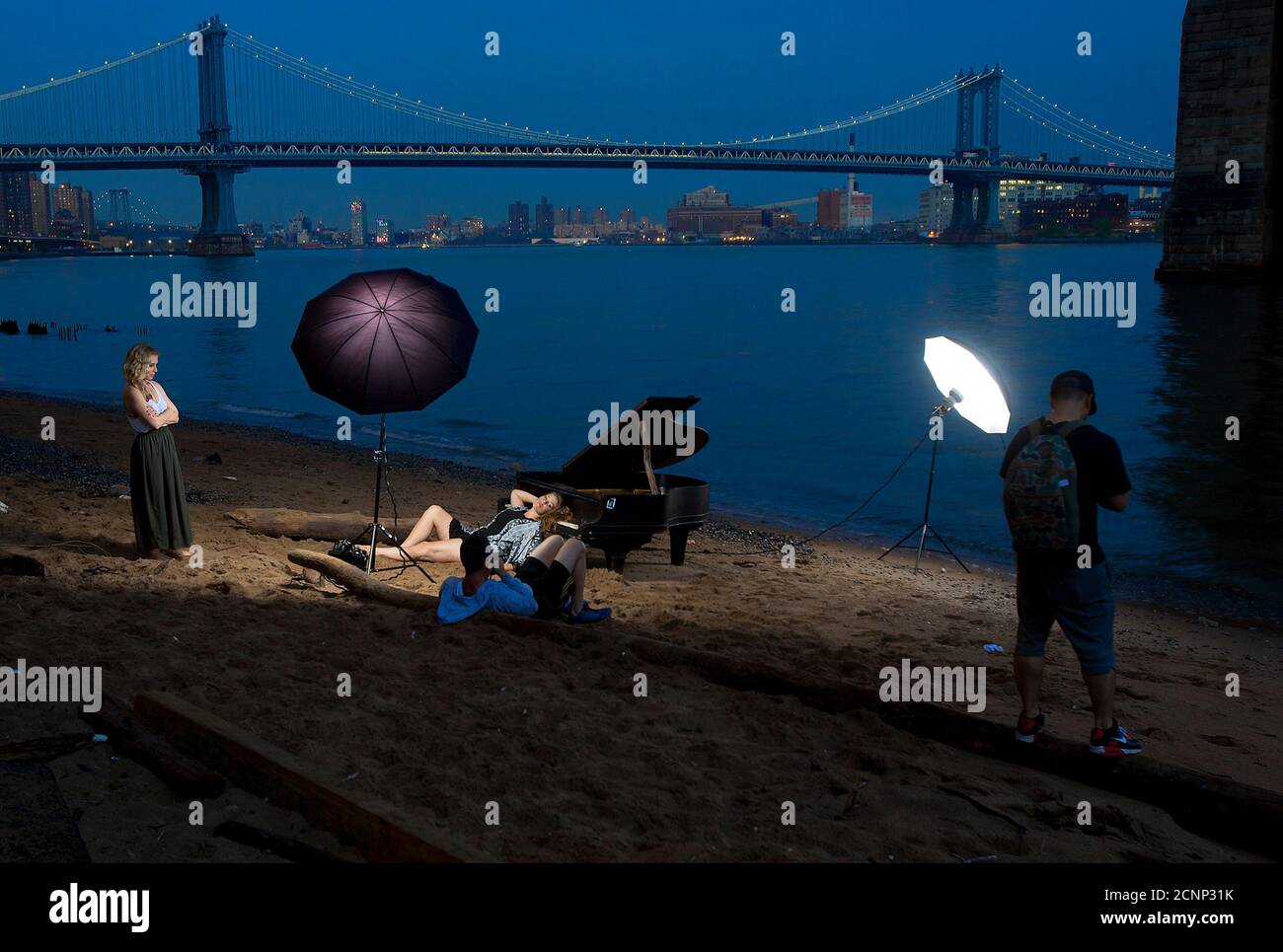 A woman poses for a photo as she leans on a grand piano that has been left beside the East River, during a fashion shoot underneath the Brooklyn Bridge in the Manhattan borough of New York June 3, 2014. According to local media, the piano had been in this space for about a week, puzzling locals as to how it got there and the reason for its placement, perfectly under the bridge.   REUTERS/Carlo Allegri (UNITED STATES - Tags: SOCIETY CITYSCAPE FASHION TPX IMAGES OF THE DAY) Stock Photo
