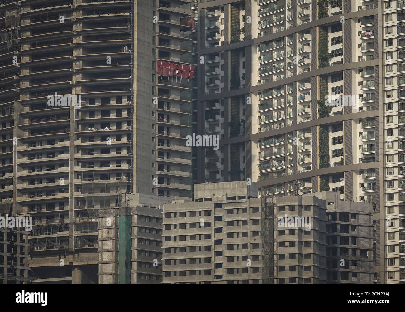 Windows of high-rise residential buildings which are under construction are  seen surrounding a residential tower (R) in central Mumbai January 12,  2015. The cost for buying a 2400 square feet (223 square