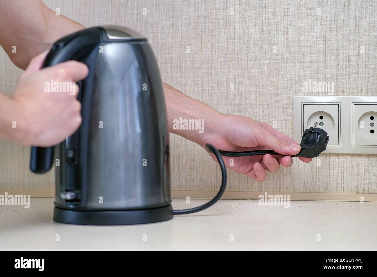 The man holds the electric power in his hand and connects the kettle to the outlet Stock Photo