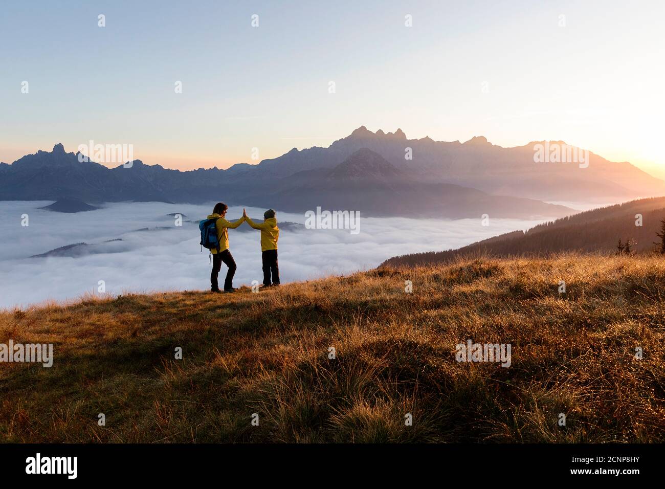 Mother and son standing on the Rossbrand mountain, giving high five at sunrise Stock Photo