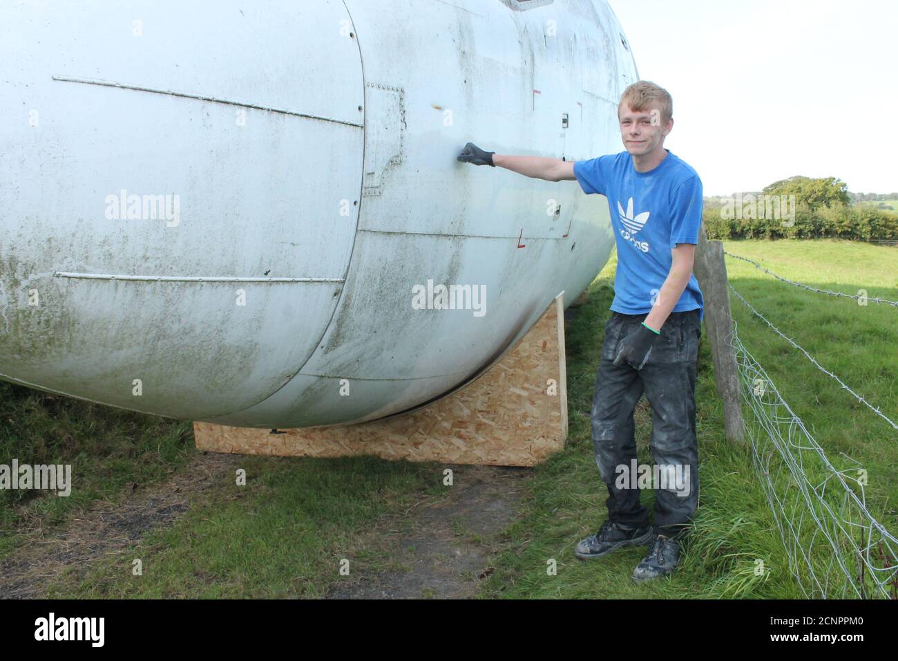 Teenager stood next to part of a boeing 737 fuselage in a farmers field UK Stock Photo