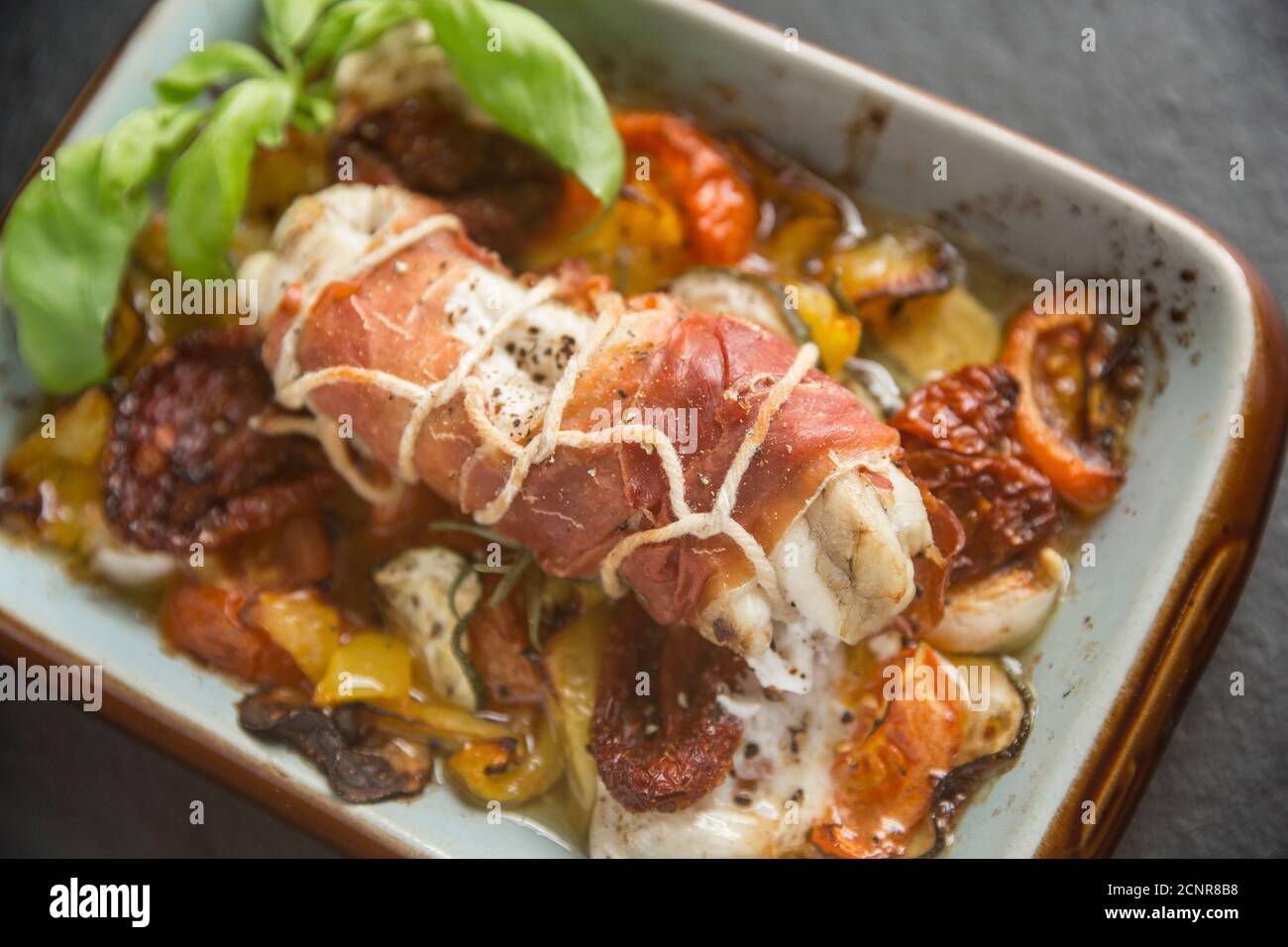 A monkfish, or anglerfish, tail, Lophius piscatorius, that has been wrapped in cured ham and roasted with vegetables and garnished with basil. Dorset Stock Photo