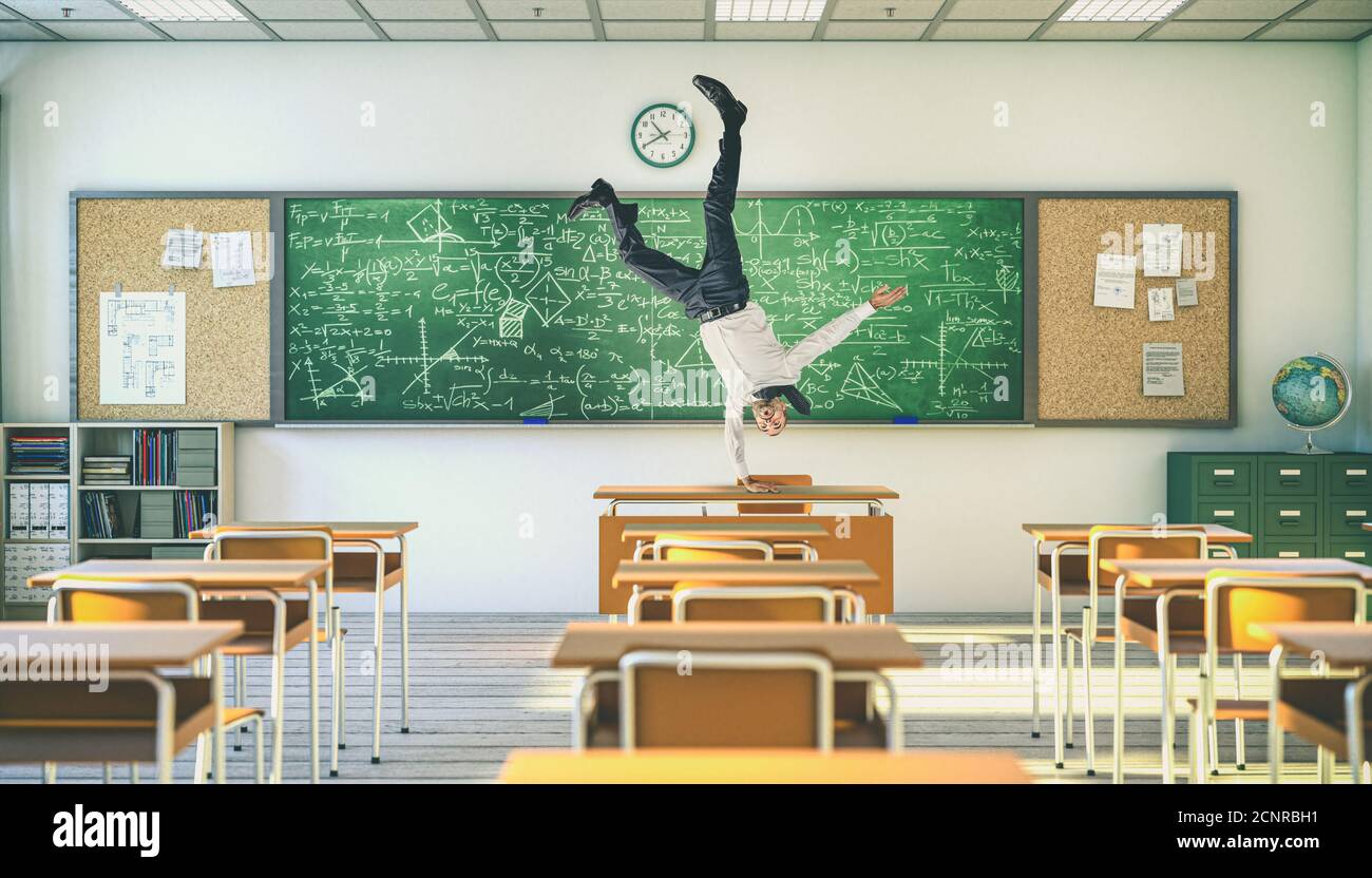 Upside-down teacher balancing on a desk inside a school classroom. Stock Photo