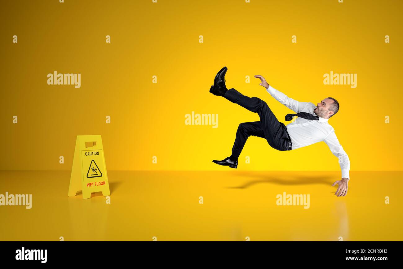 businessman slips on wet floor, caution sign in sight, yellow background. Stock Photo