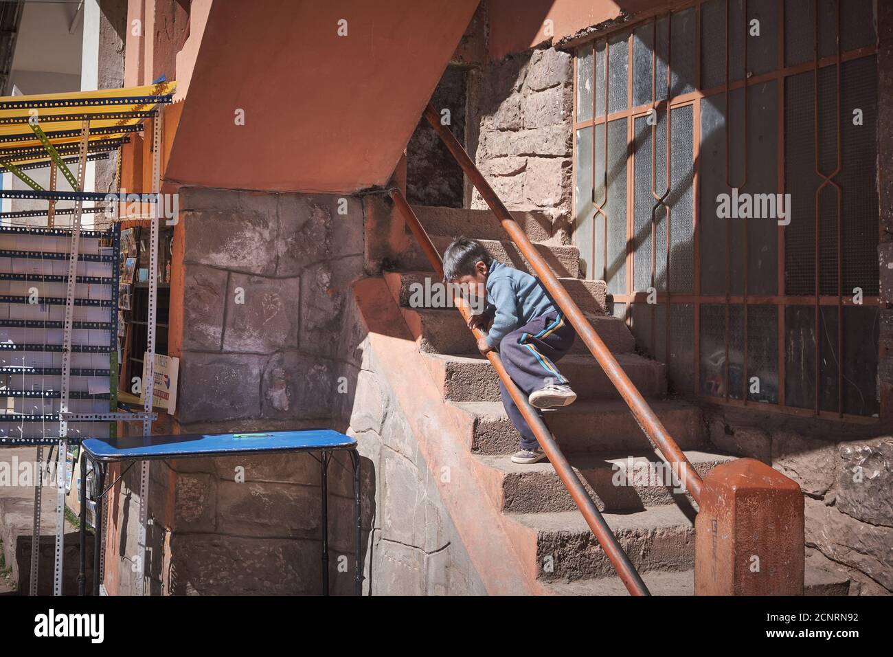 A young boy child plays on the handrails of some steps stairs in the main village of Taquile Island, Lake Titicaca, Peru Stock Photo