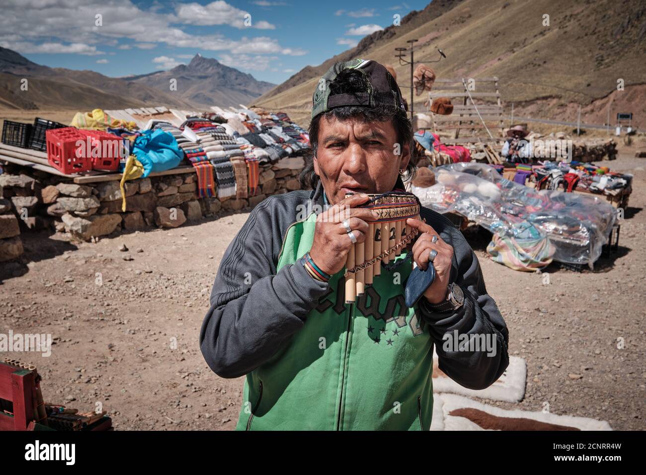 A market trader demonstrating pan pipes panpipes pan-pipes syrinx at a roadside market in the Altiplano high Andes, Peru, selling textiles and fabrics Stock Photo