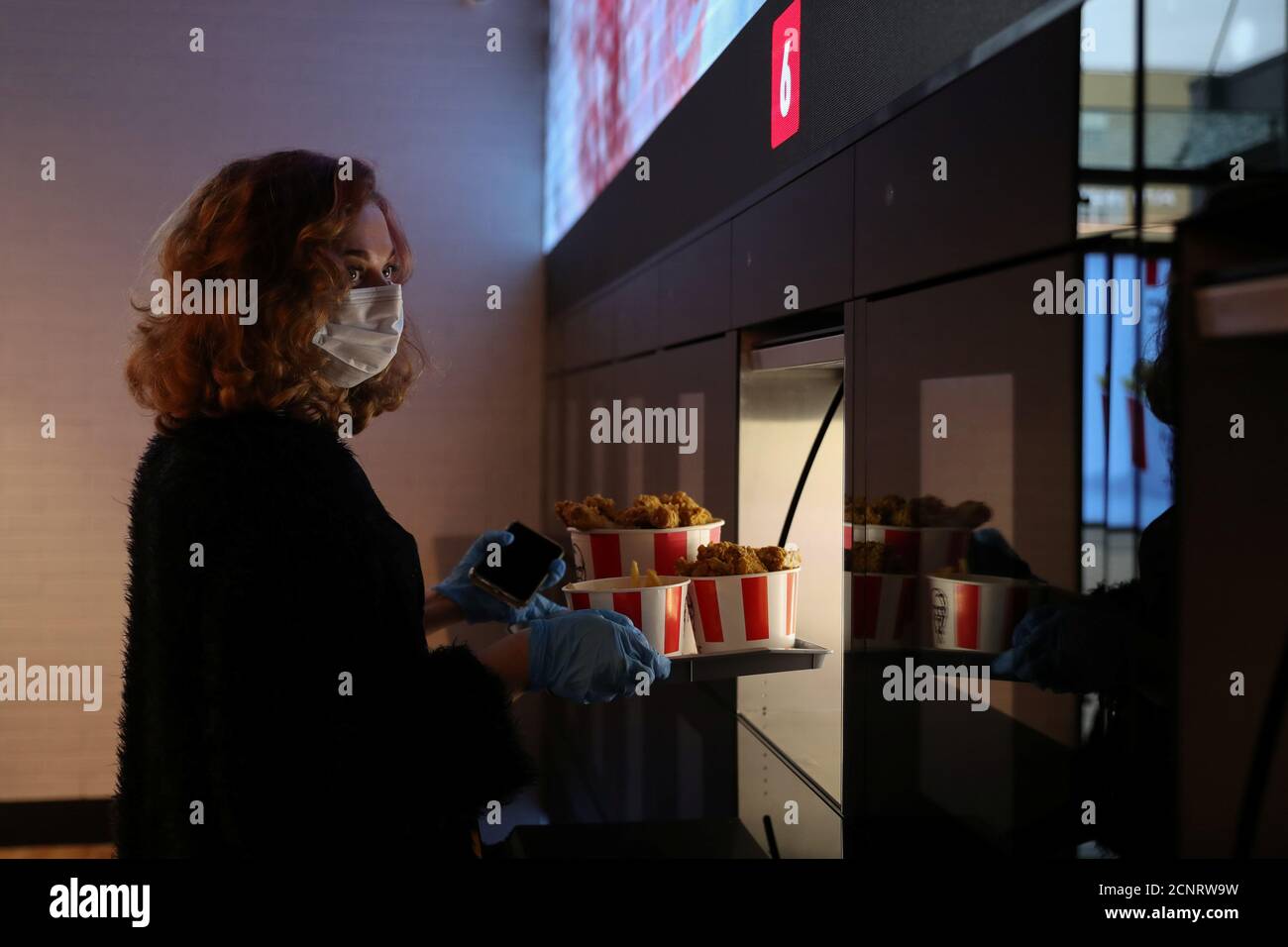 An employee wearing a protective face mask and gloves picks up a tray of food from a cubby, which opens automatically with a facial recognition system, at a KFC restaurant offering contactless service, ahead of its opening following the easing of restrictions implemented to curb the spread of the coronavirus disease (COVID-19) in Moscow, Russia June 21, 2020. REUTERS/Evgenia Novozhenina Stock Photo