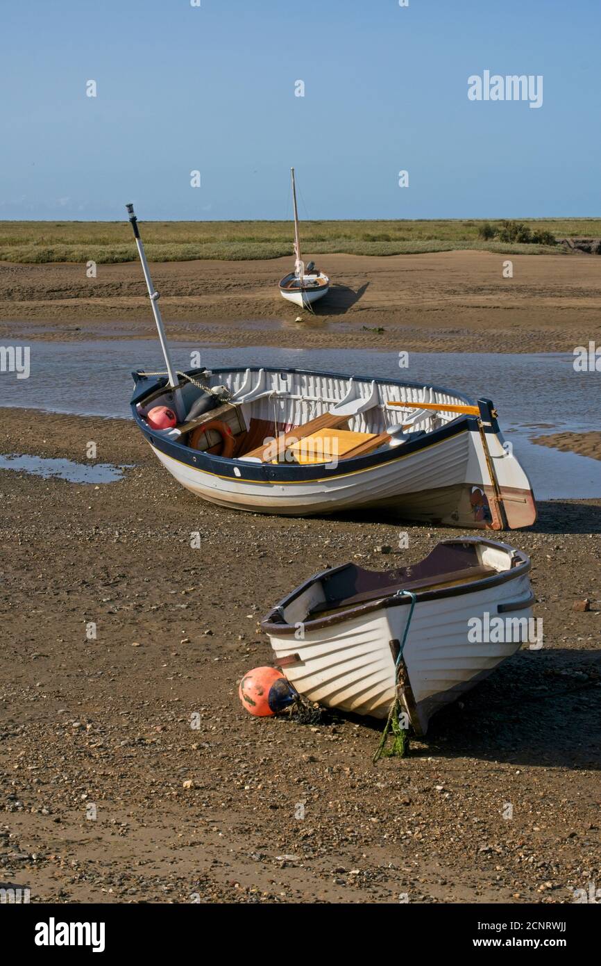 Trio of traditional boats moored high and dry foreground to background on sand banks of estuary. Clear blue sky.   Portrait format. Stock Photo