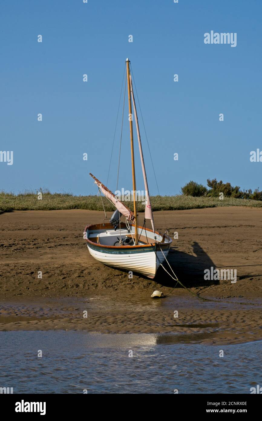 Traditional sailing boat moored high and dry at low tide on sand banks of estuary. Clear blue sky. Burnham Overy, Norfolk.  Portrait format. Stock Photo