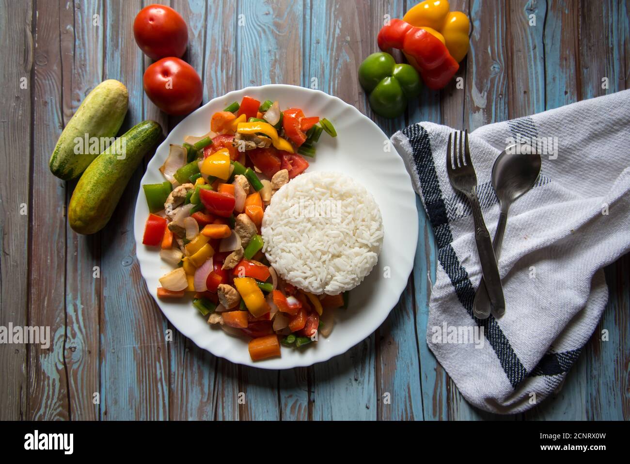 Steamed rice along with chicken and vegetables saute in a white plate with ingredients on a background Stock Photo
