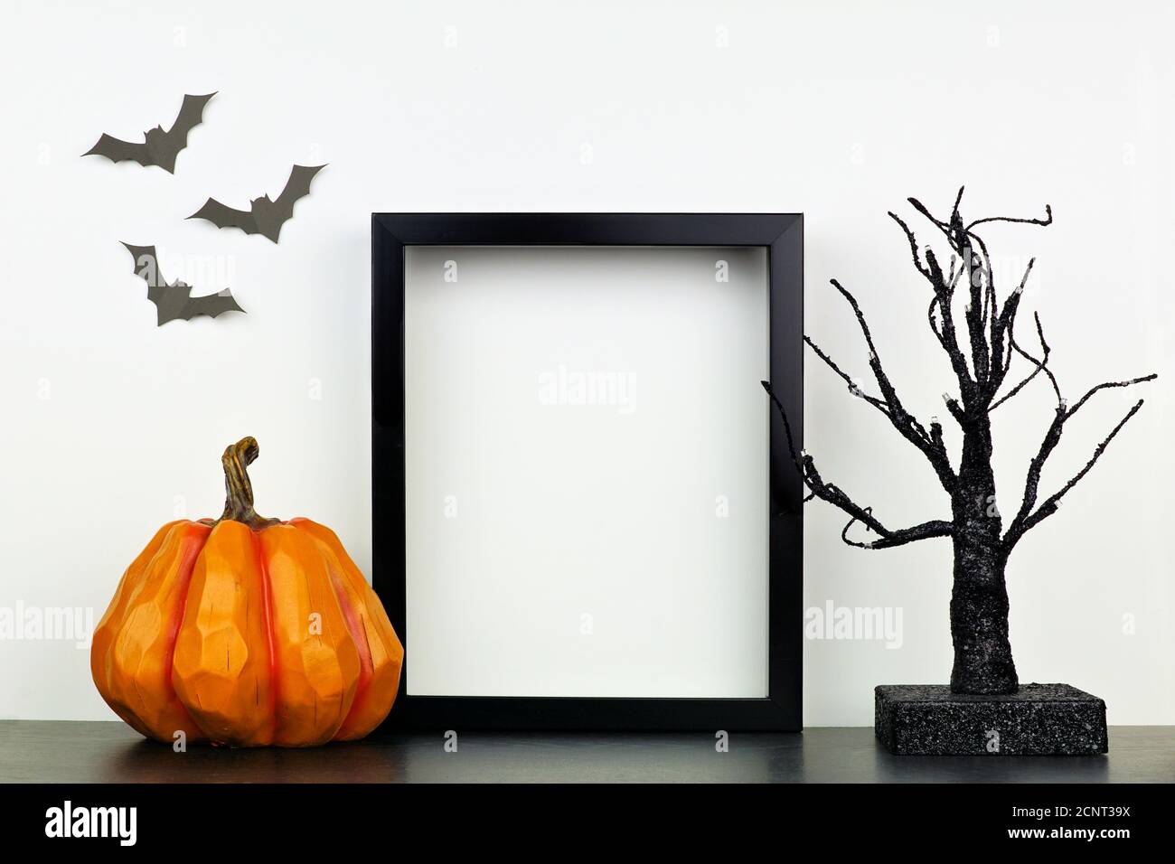 Mock up black frame with pumpkin and spooky tree decor on a shelf or desk. Halloween concept. Portrait frame against a white wall with bats. Stock Photo