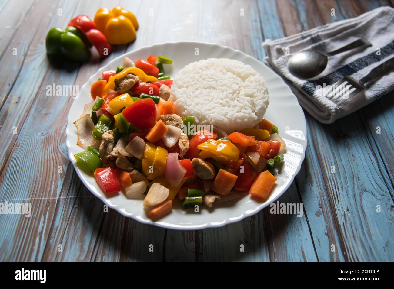 Rice along with chicken and vegetables saute in a white plate with ingredients on a background Stock Photo