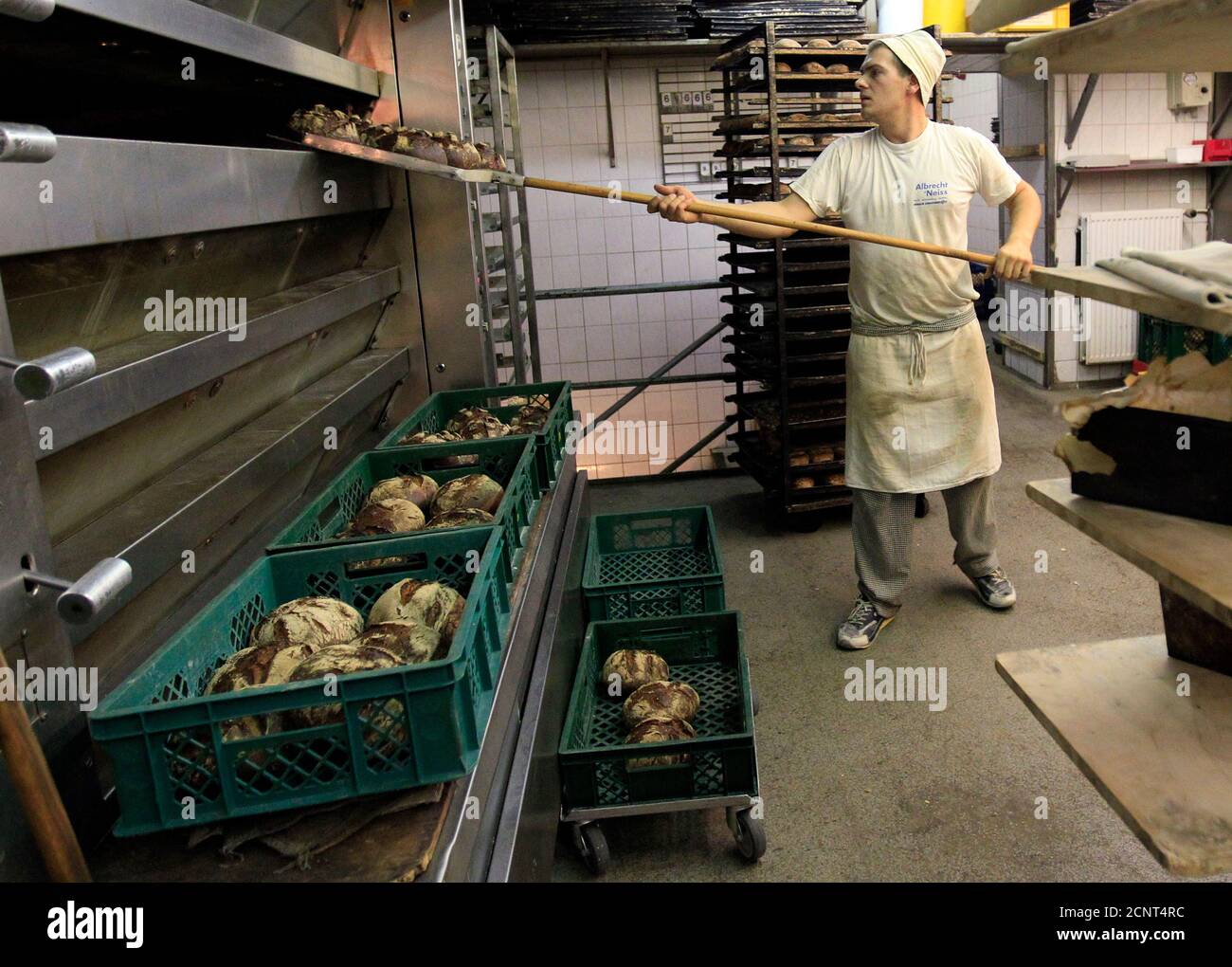 A man takes loaves of bread out of an oven in a bakery in Berlin August 26, 2010.  Germany's 2010 grain crop of all types is likely to fall to around 43.9 million tonnes from 49.7 million tonnes last year, German farmers' association DBV said on Wednesday. German grain has suffered from an early summer heatwave followed by heavy harvest-time rain, it said.  REUTERS/Thomas Peter (GERMANY - Tags: BUSINESS FOOD AGRICULTURE) Stock Photo