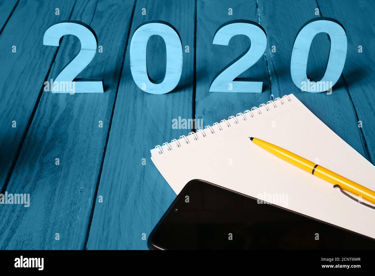 Planing concept idea for 2020 year. Twenty twenty, smart phone and notebook blank space with yellow pen on wooden surface blue color. Stock Photo
