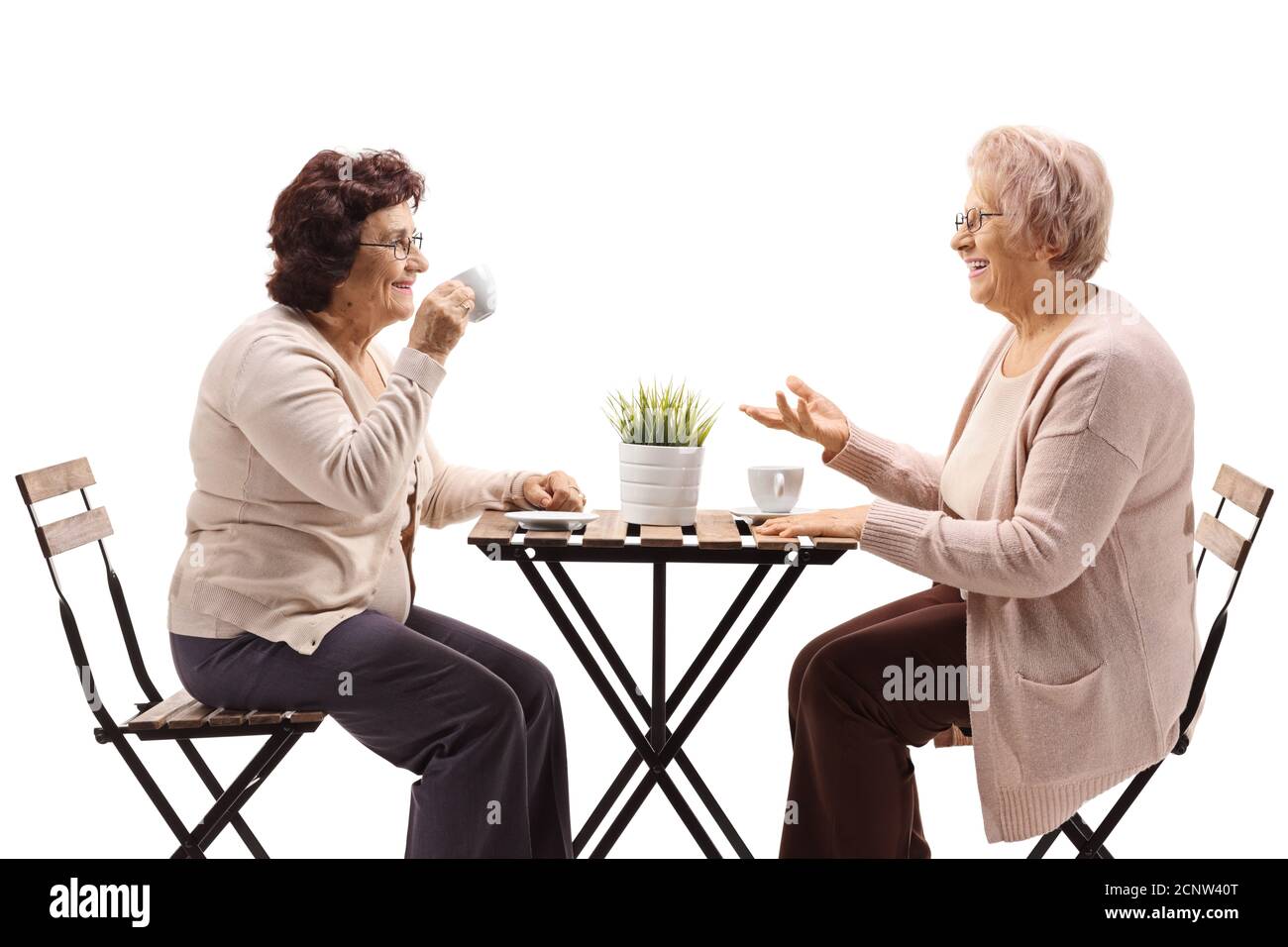 Elderly female friends drinking coffee at a table and talking isolated on white background Stock Photo