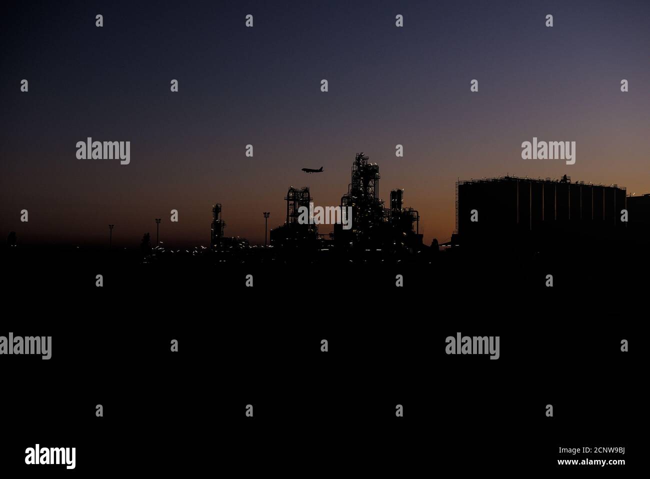 Industrianlage bei Sonnenuntergang mit Mondsichel und Flugzeug Stock Photo