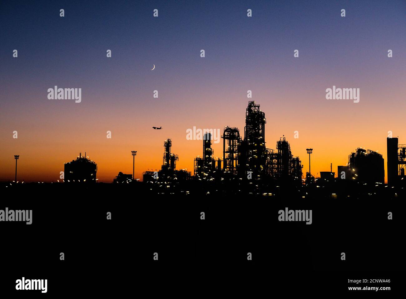 Industrianlage bei Sonnenuntergang mit Mondsichel und Flugzeug Stock Photo