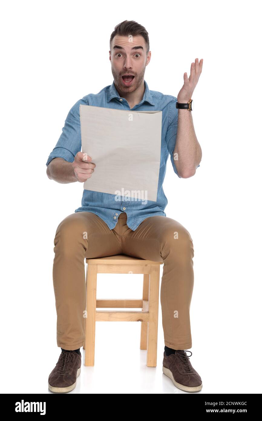 Amazed smart casual man reading newspaper and shouting while sitting on ...