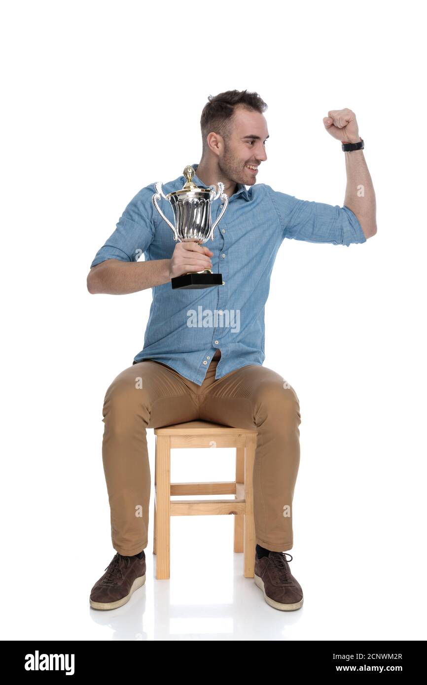 Cheerful smart casual man holding trophy and celebrating while sitting ...
