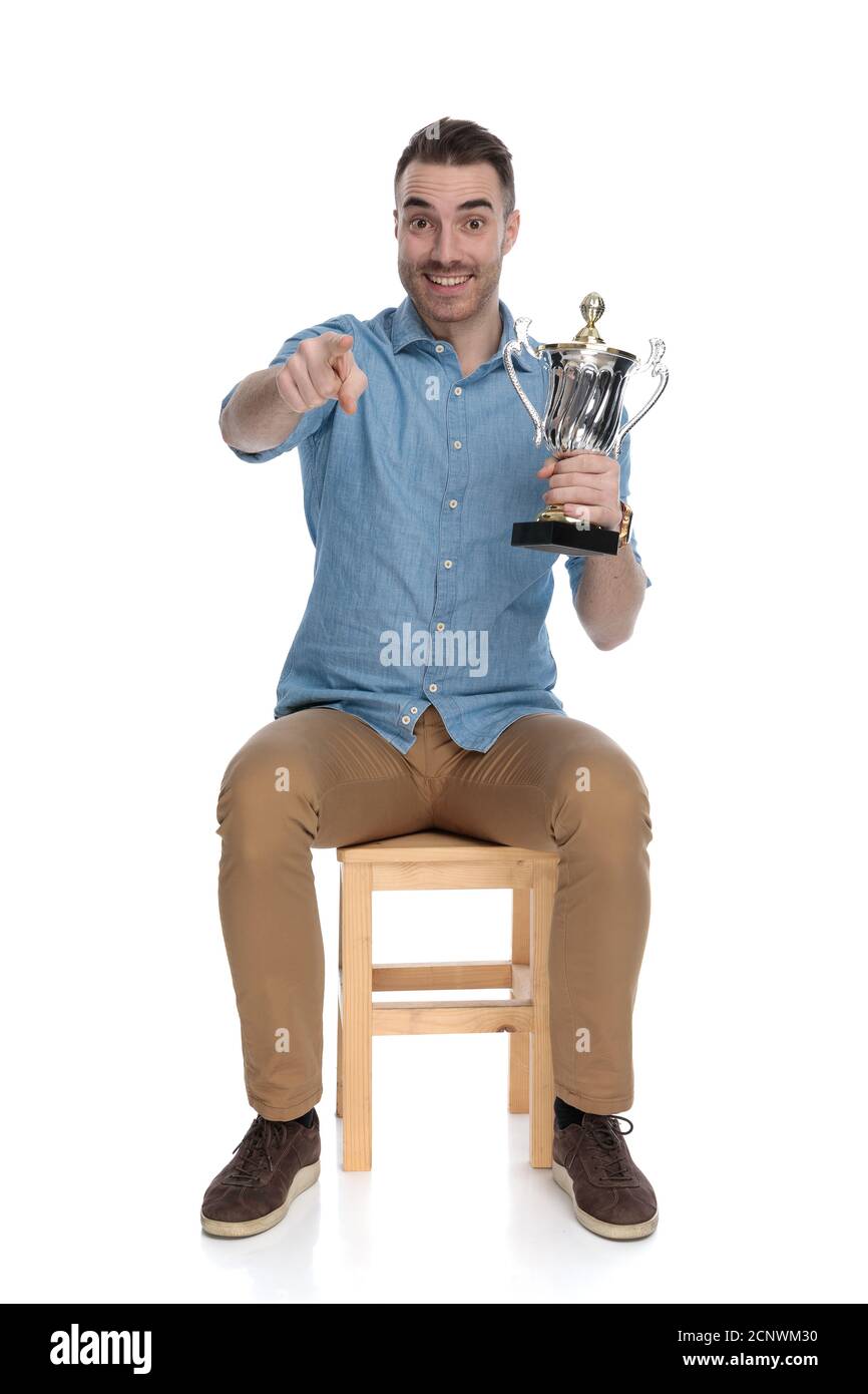Positive smart casual man holding trophy and pointing forward while ...