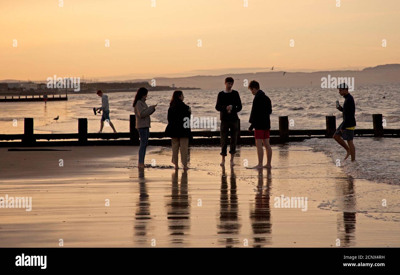 Portobello Beach, Edinburgh, Scotland, UK. 18 September 2020. Temperature 15 degrees. Evening at Portobello Beach after a busy day at the seaside things quitened off once the hazy sun was going down, a few students cycle towards the prom, one very smoky barbeque and two Irish lassies who work in Edinburgh exit from a bracing evening dip in the Firth of Forth. Credit: Scottishcreative/ Alamy Live News. Stock Photo