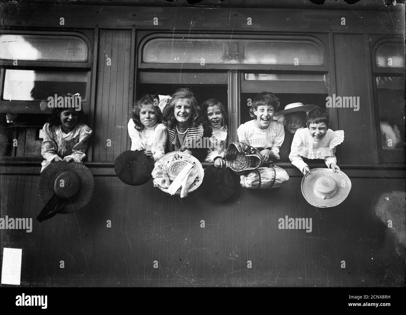 Girls holding hats leaning out a train window before leaving for summer camp, Chicago, Illinois Stock Photo