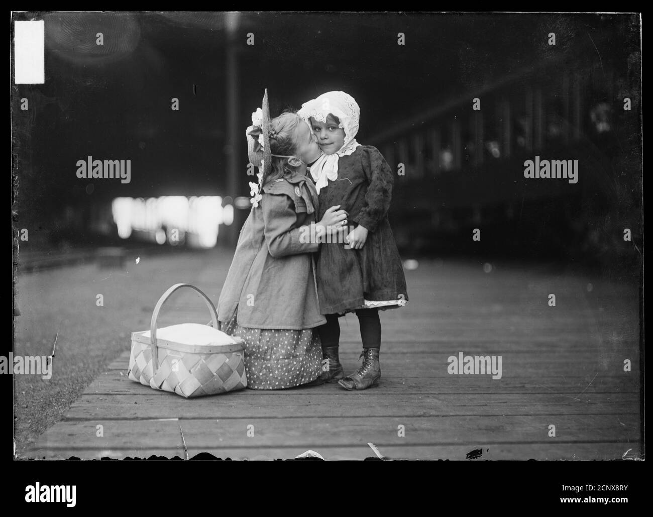 Image of a girl kneeling to kiss a younger girl on the cheek, on a train platform in Chicago, Illinois, before leaving for summer camp Stock Photo