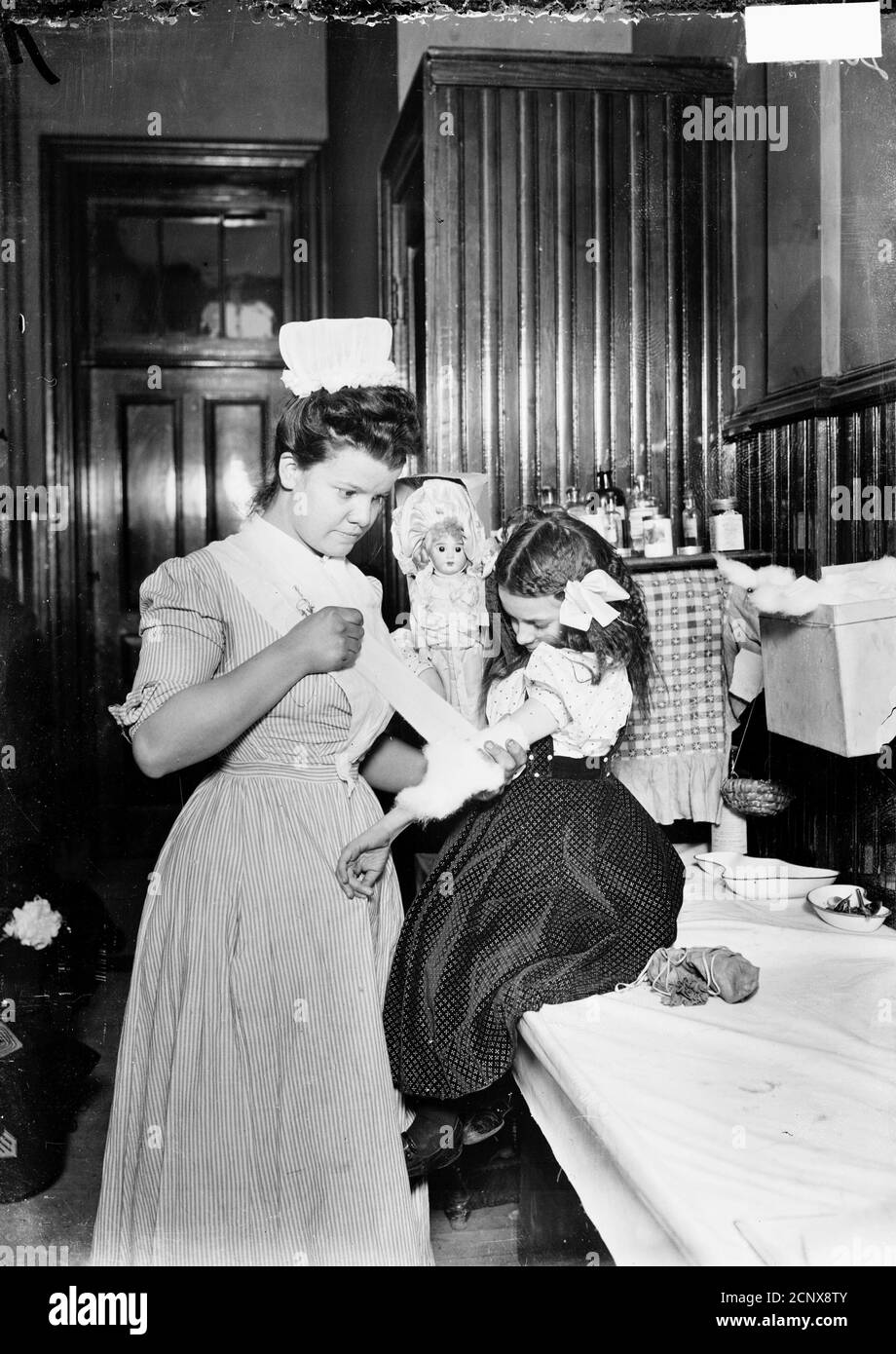 Image of a nurse bandaging a girl's arm in a room in Chicago, Illinois, circa 1905. Stock Photo