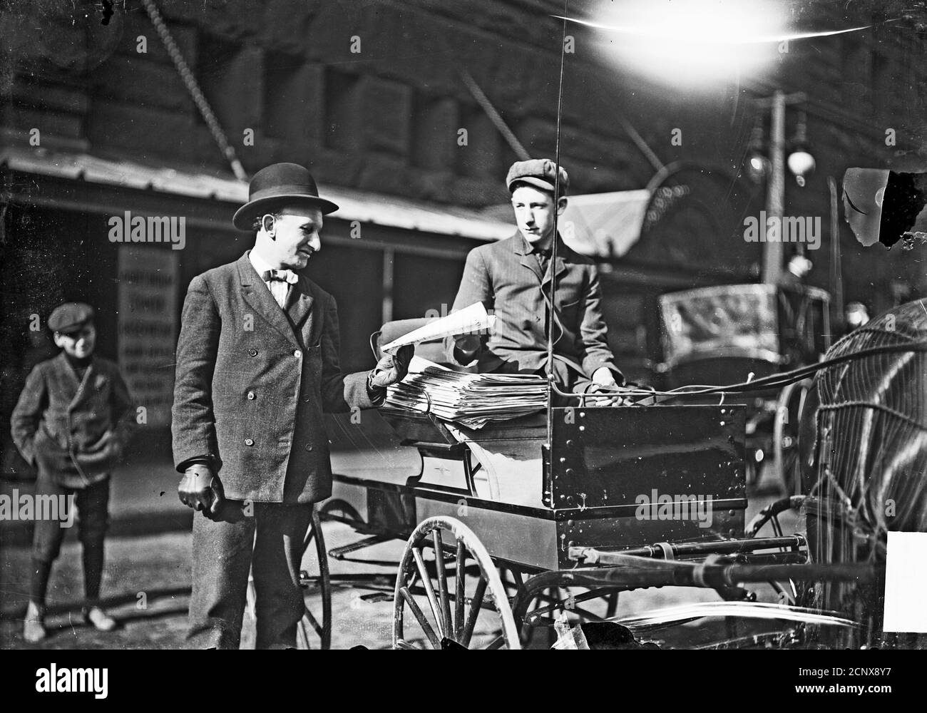 Image of a newsboy with a disability in a horse-drawn cart at the side of a street in Chicago, Illinois, handing a man a paper. Stock Photo