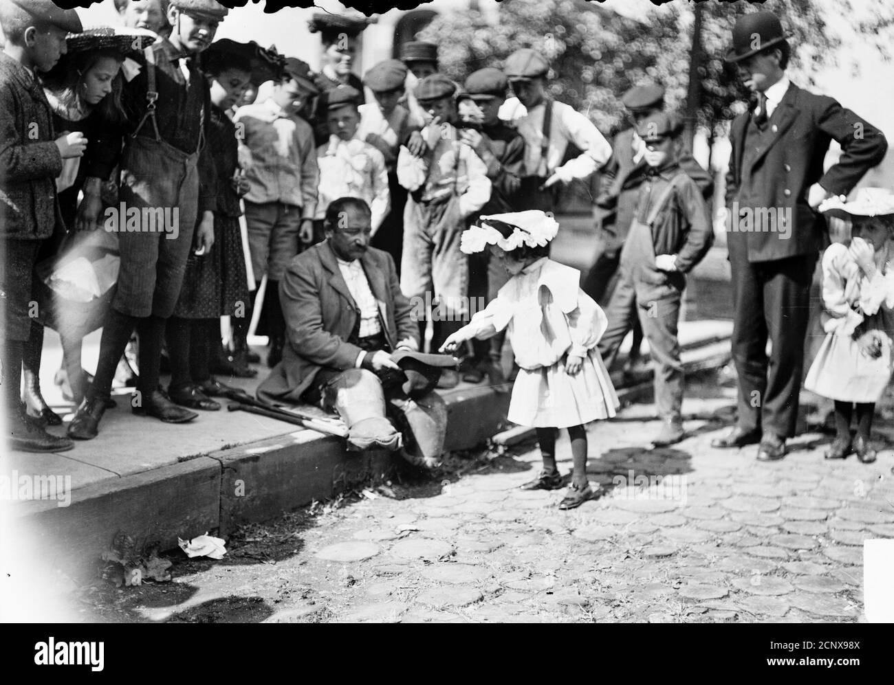 Amputee holding out his hat to a little girl who is dropping a coin into it, possibly in front of St. Joseph Roman Catholic Church, Chicago, Illinois Stock Photo