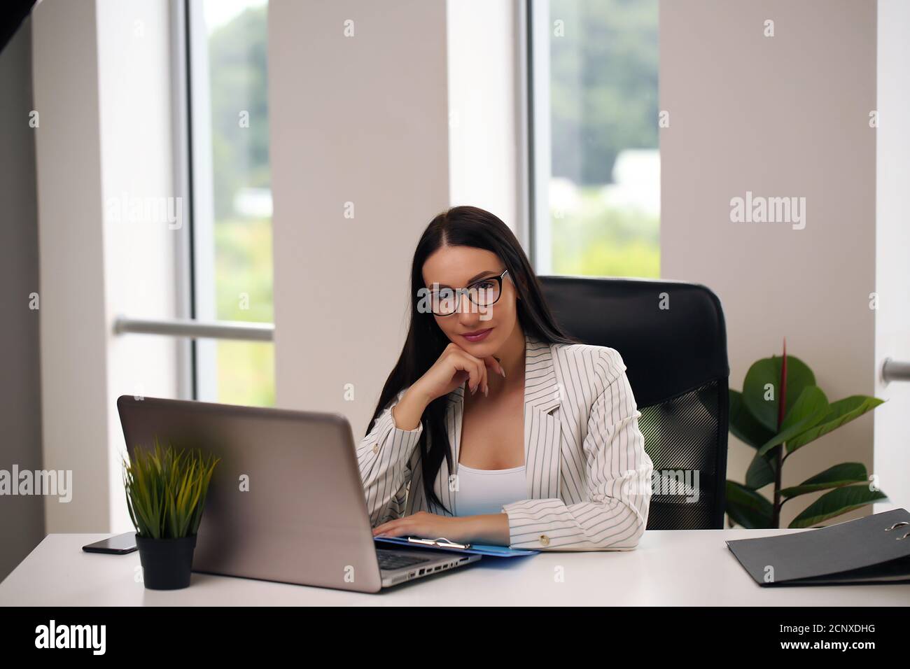 Portrait of smiling pretty young business woman in glasses sitting on ...
